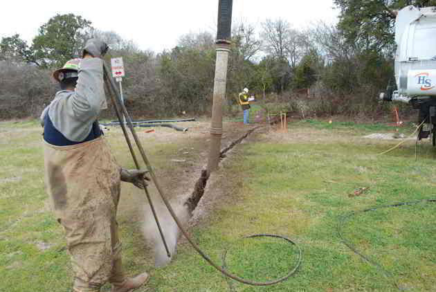 Hydro excavation operator using vacuum hose to recover spoils from a trench